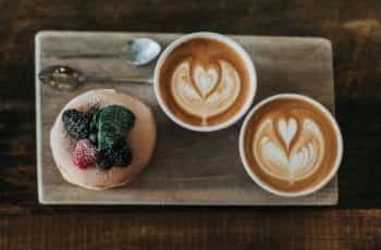 A puff pastry and two coffee mugs placed on a wooden serving tray.