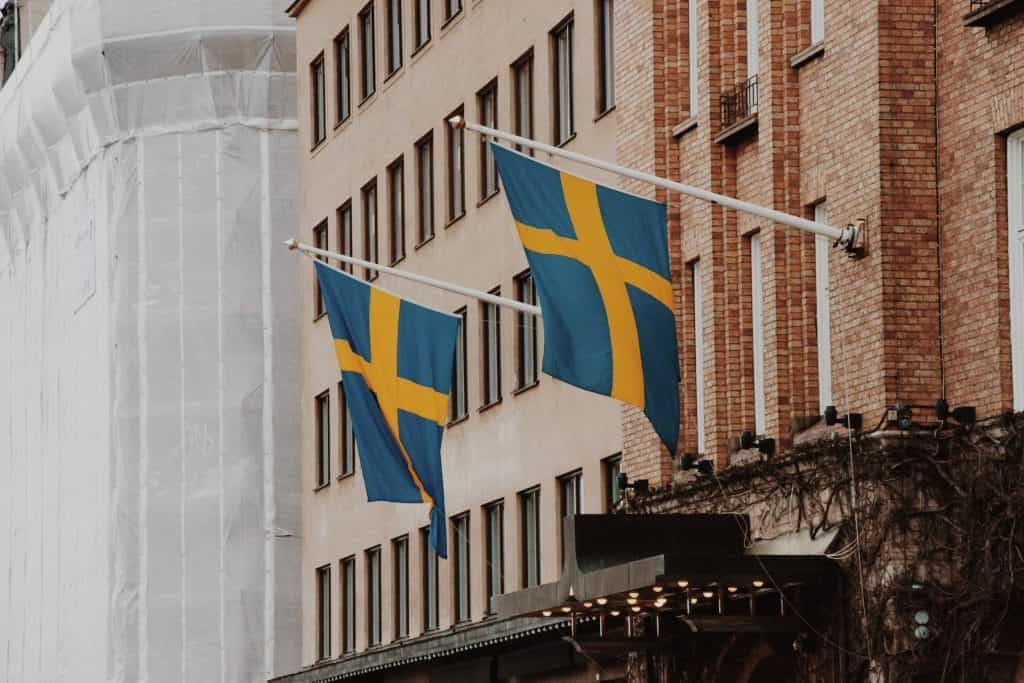 Two Swedish flags danging from poles on the side of a building.