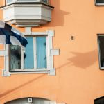 A white and blue flag in front of a window of a brown building.